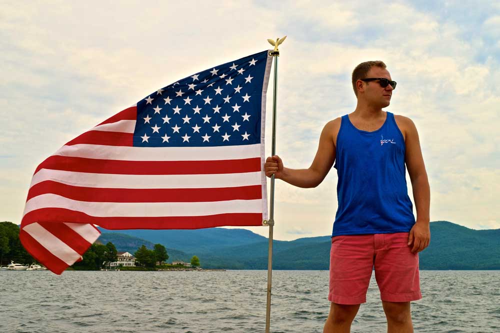 man in blue poses with american flag on lake george