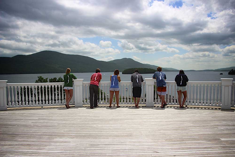 six people leaning on gate with lake george in backdrop